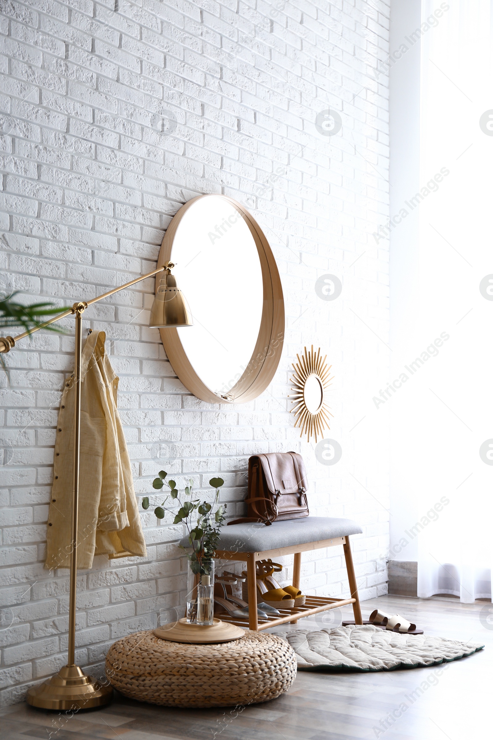 Photo of Hallway interior with big round mirror and shoe storage bench near brick wall