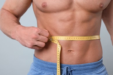 Photo of Athletic man measuring waist with tape on light grey background, closeup. Weight loss concept