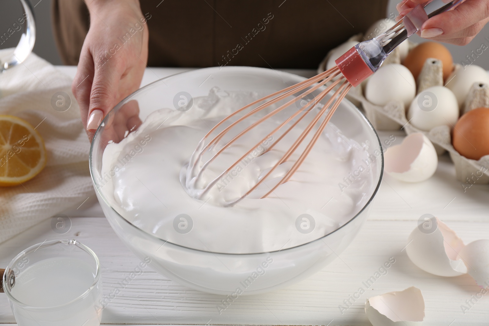 Photo of Woman making whipped cream with whisk at white wooden table, closeup