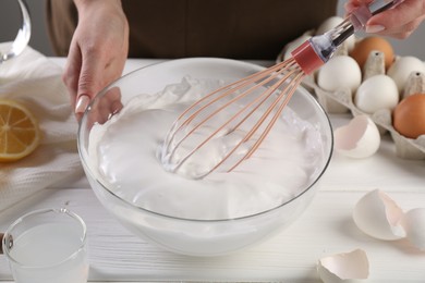 Woman making whipped cream with whisk at white wooden table, closeup