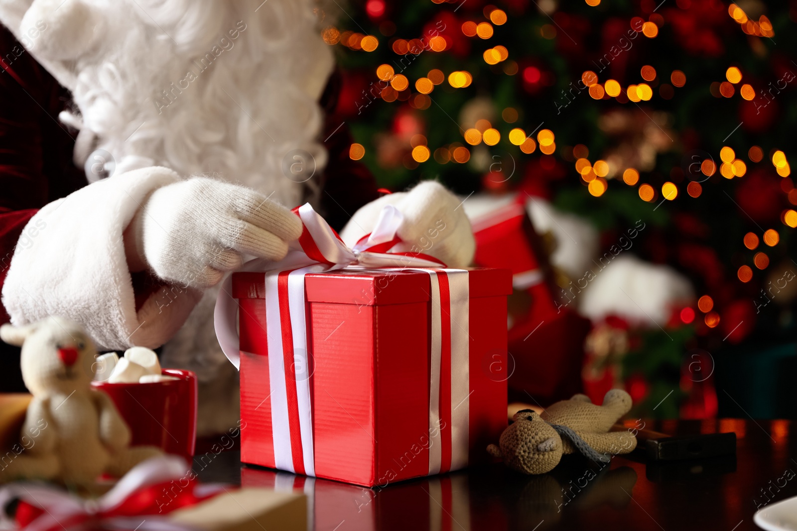 Photo of Santa Claus wrapping Christmas gift against blurred festive lights, closeup