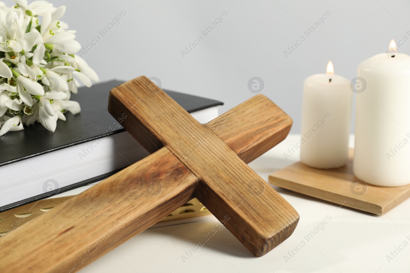 Photo of Wooden cross, ecclesiastical books, church candles and flowers on white table, closeup