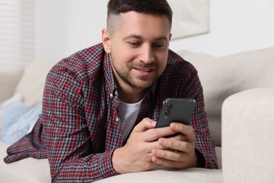 Photo of Handsome man sending message via smartphone on sofa at home