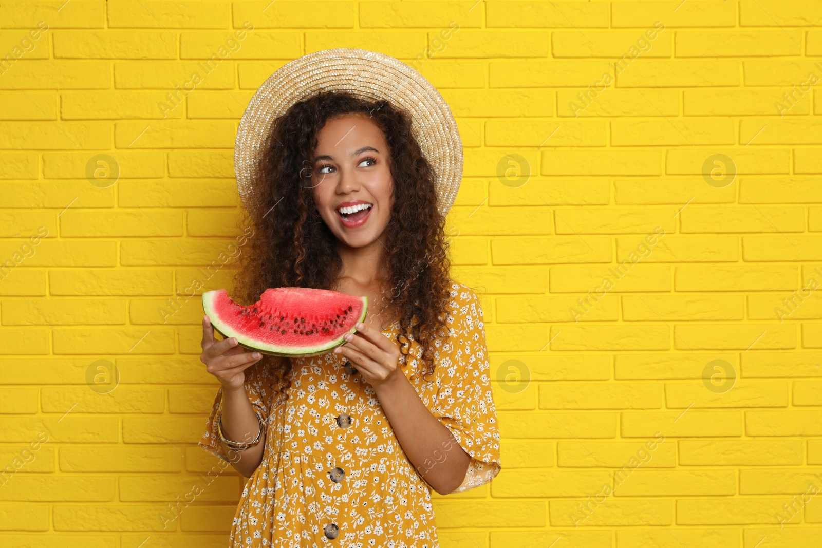 Photo of Beautiful young African American woman with watermelon near yellow brick wall. Space for text