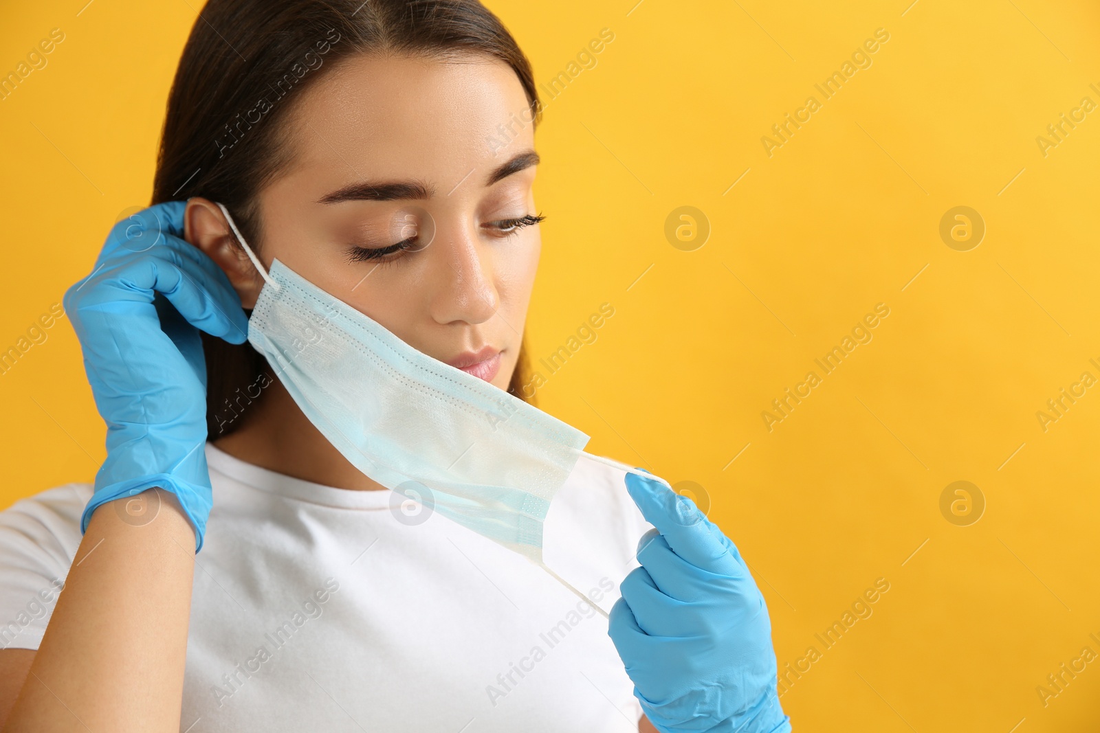 Photo of Woman in medical gloves putting on protective face mask against yellow background. Space for text