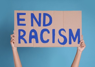 Woman holding sign with phrase End Racism on light blue background, closeup