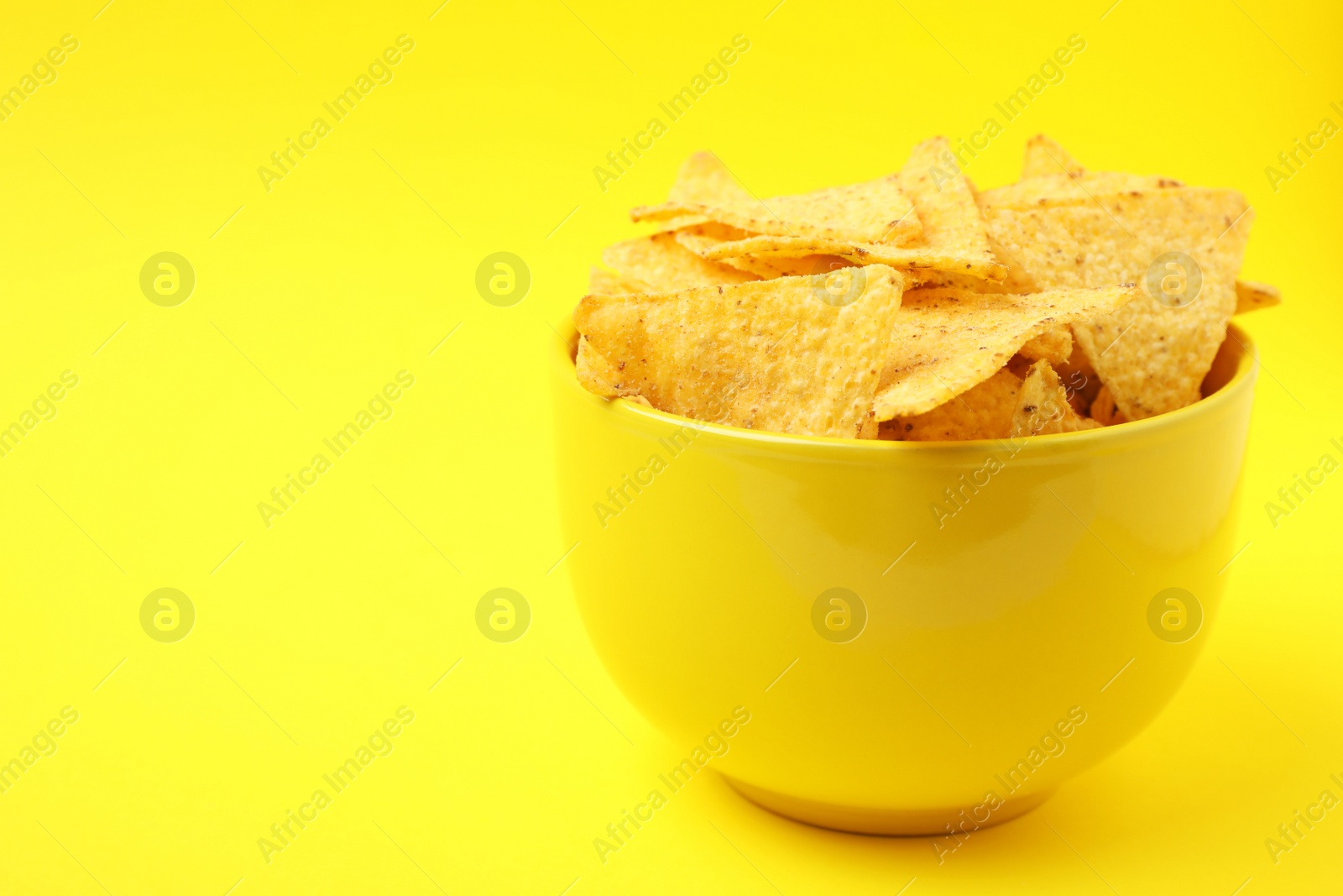 Photo of Bowl of tasty Mexican nachos chips on yellow background. Space for text