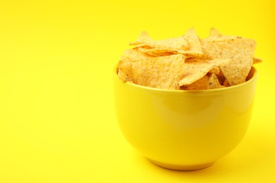 Photo of Bowl of tasty Mexican nachos chips on yellow background. Space for text