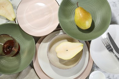 Stylish ceramic plates, glass, cutlery and pears on white marble table, flat lay