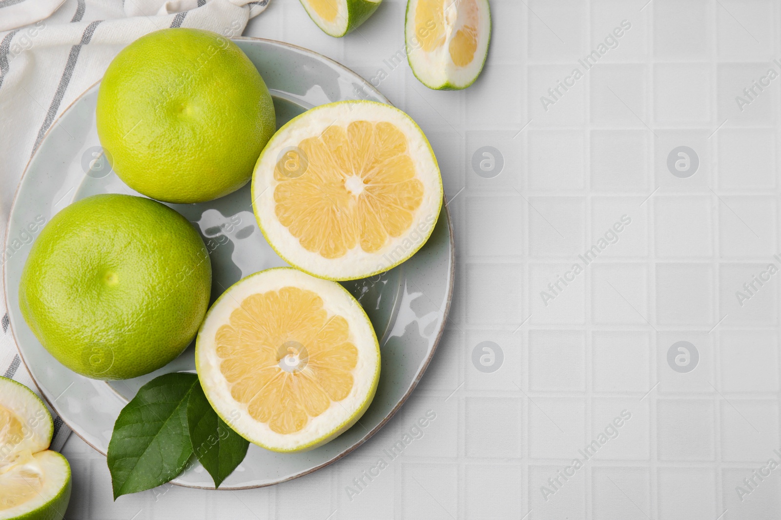 Photo of Whole and cut sweetie fruits with green leaves on white tiled table, flat lay. Space for text