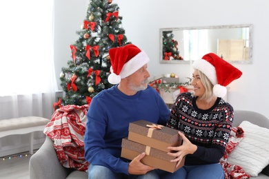 Photo of Mature couple in Santa hats with Christmas gift boxes at home