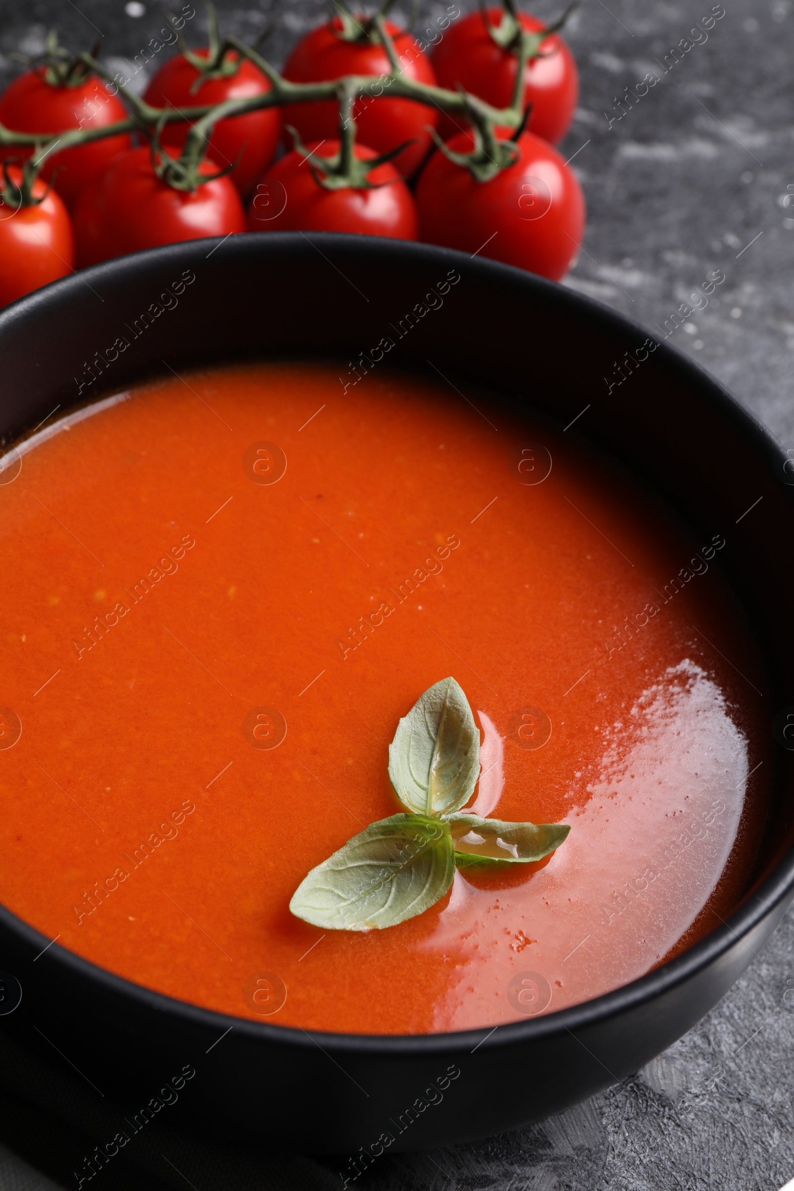 Photo of Delicious tomato cream soup in bowl on dark textured table, closeup