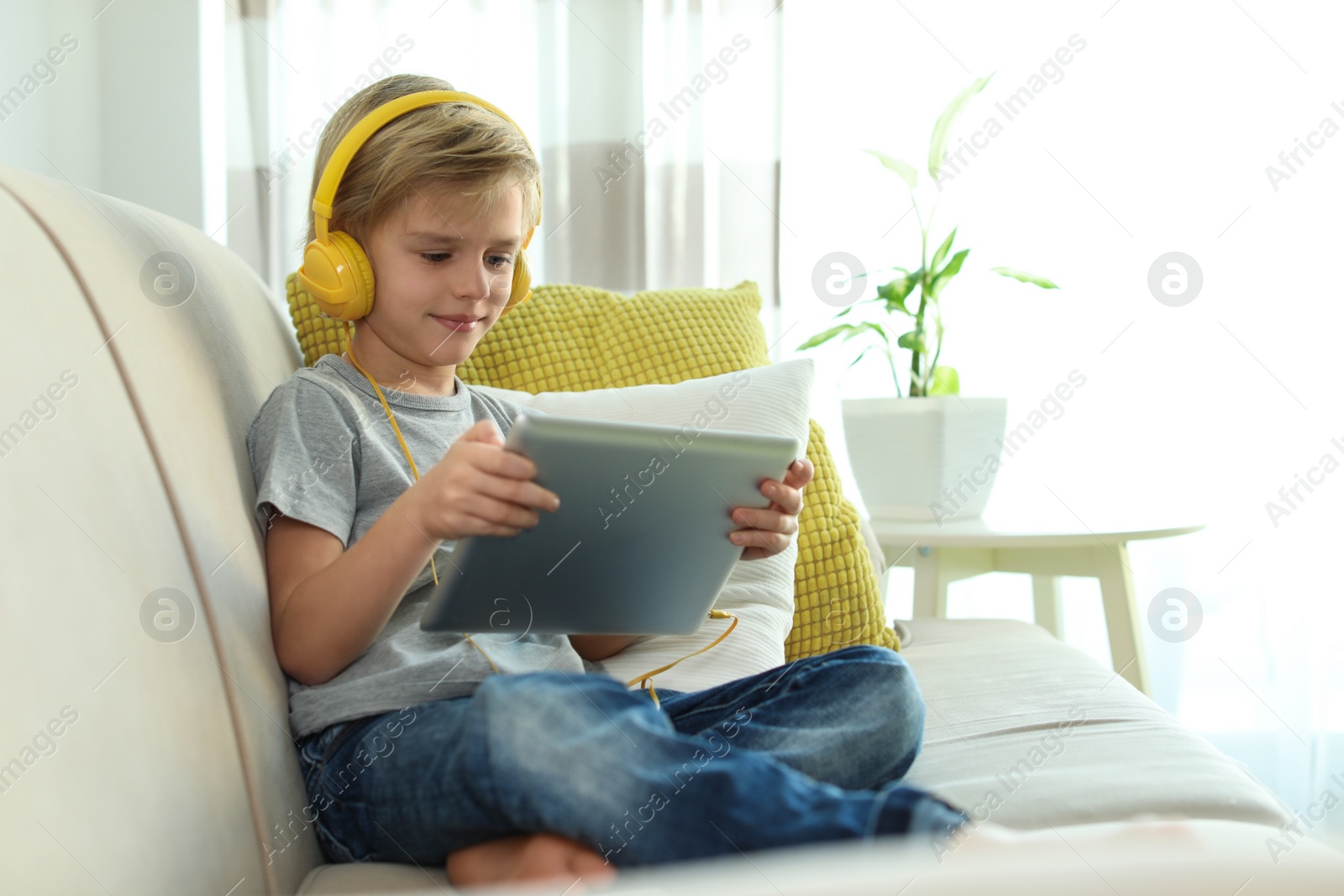 Photo of Cute little boy with headphones and tablet listening to audiobook at home