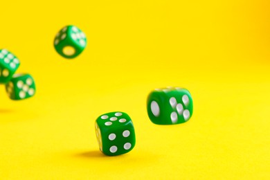 Photo of Many green game dices falling on yellow background, closeup
