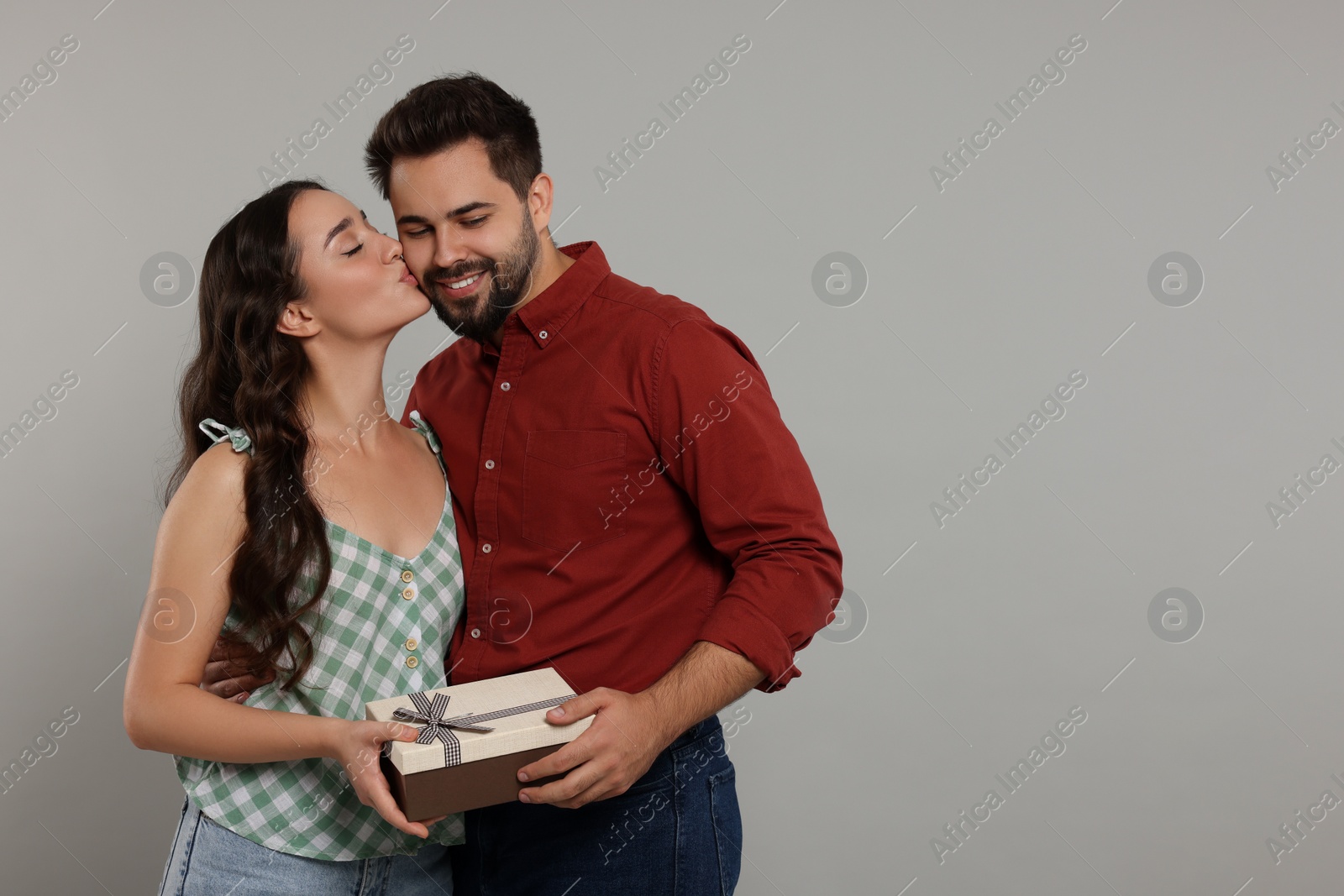 Photo of Woman kissing her smiling boyfriend on grey background, space for text. Celebrating holiday