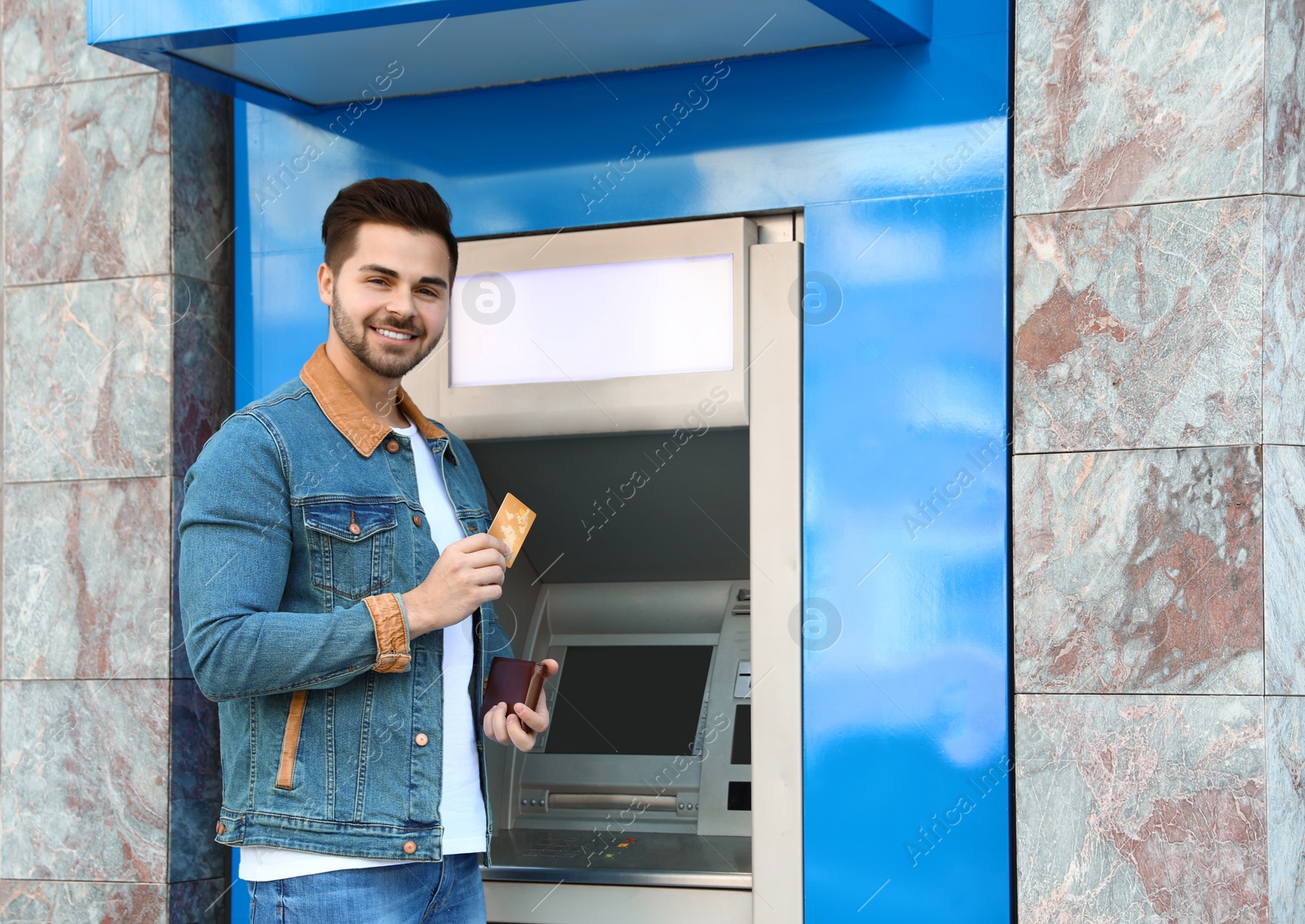 Photo of Young man with credit card near cash machine outdoors