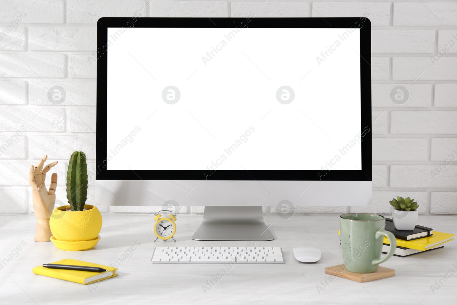 Photo of Office workplace with computer, stationery, cup and houseplants on light table near white brick wall