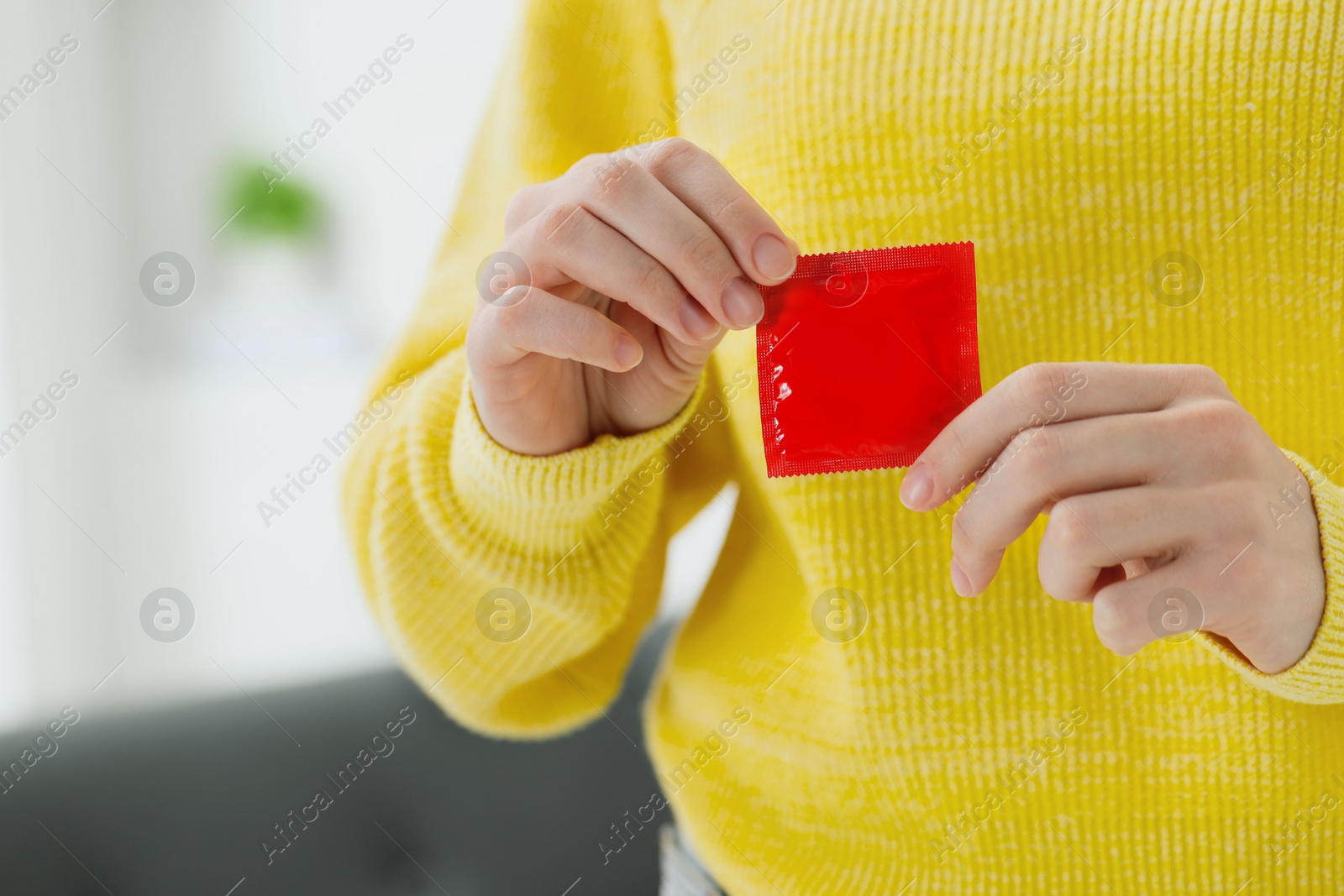 Photo of Woman holding condom indoors, closeup. Safe sex