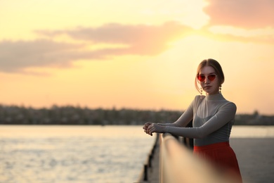 Photo of Young woman posing near railing on waterfront at sunset