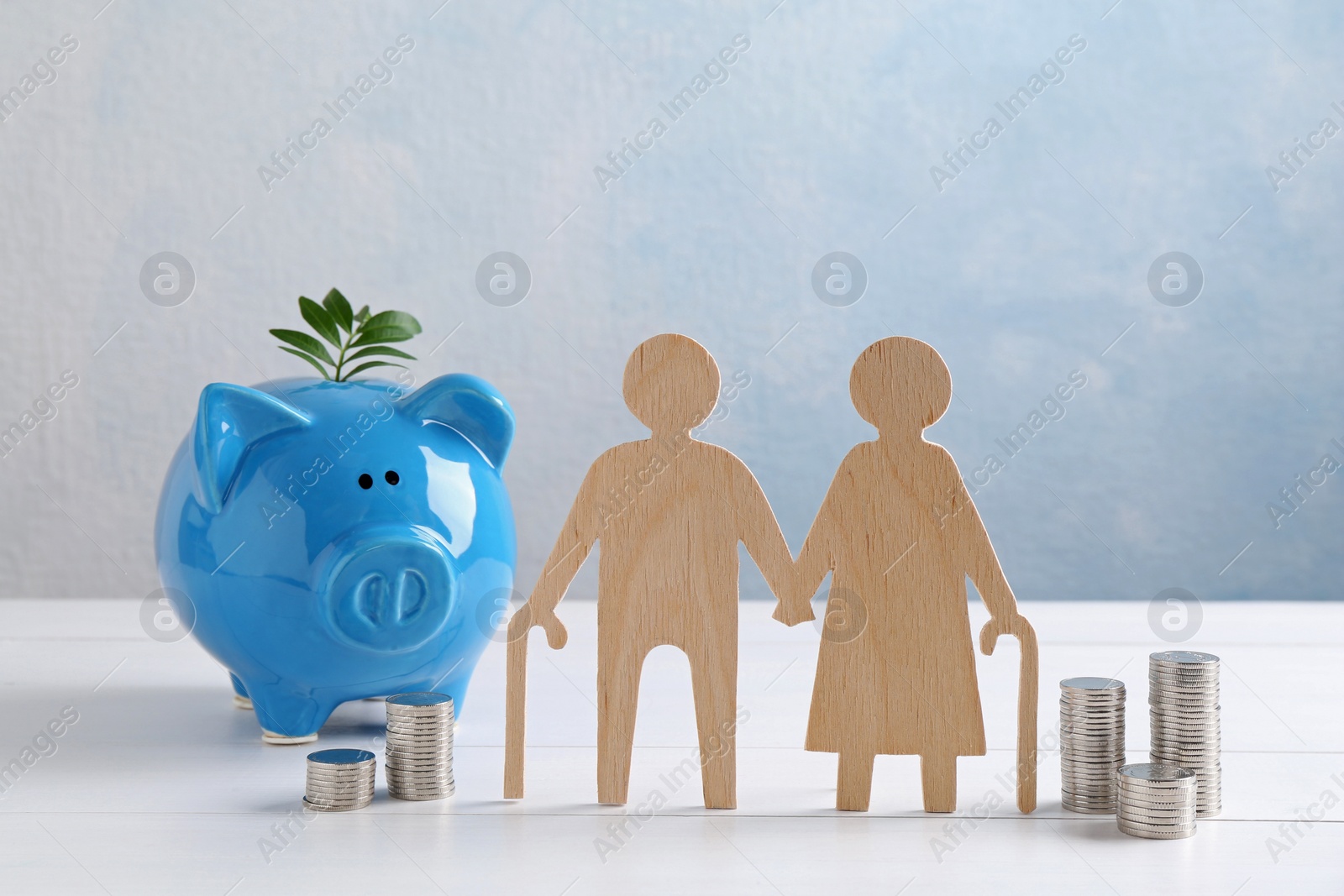 Photo of Pension savings. Figure of senior couple, stacked coins, piggy bank and green twig on white wooden table