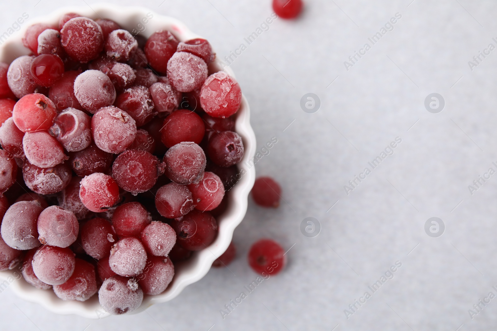 Photo of Frozen red cranberries in bowl on light table, top view. Space for text