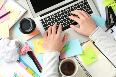 Photo of Man using laptop at messy table, top view. Concept of being overwhelmed by work