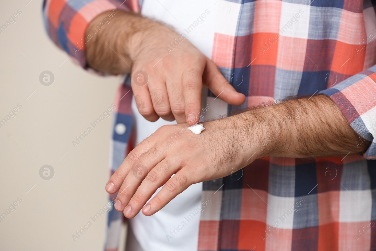 Photo of Man applying cream onto hand on beige background, closeup