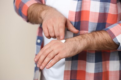 Photo of Man applying cream onto hand on beige background, closeup