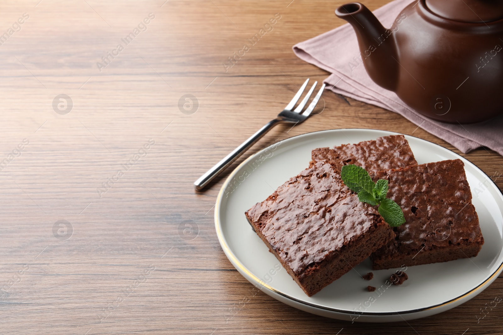 Photo of Delicious chocolate brownies with fresh mint served on wooden table. Space for text