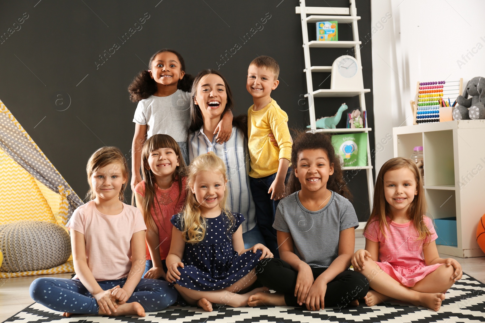 Photo of Cute little children with nursery teacher sitting on floor in kindergarten. Indoor activity