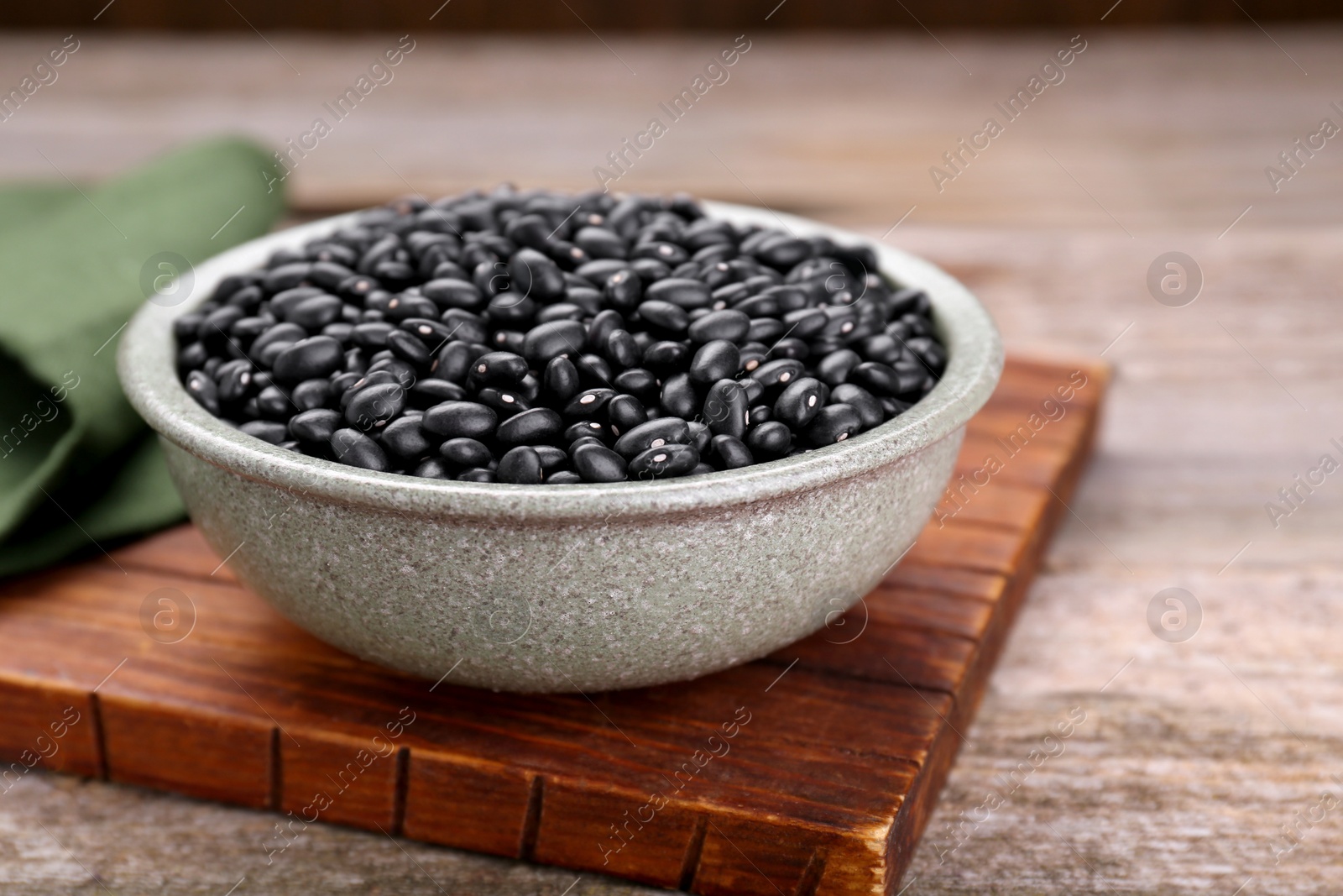 Photo of Bowl of raw black beans on wooden table, closeup