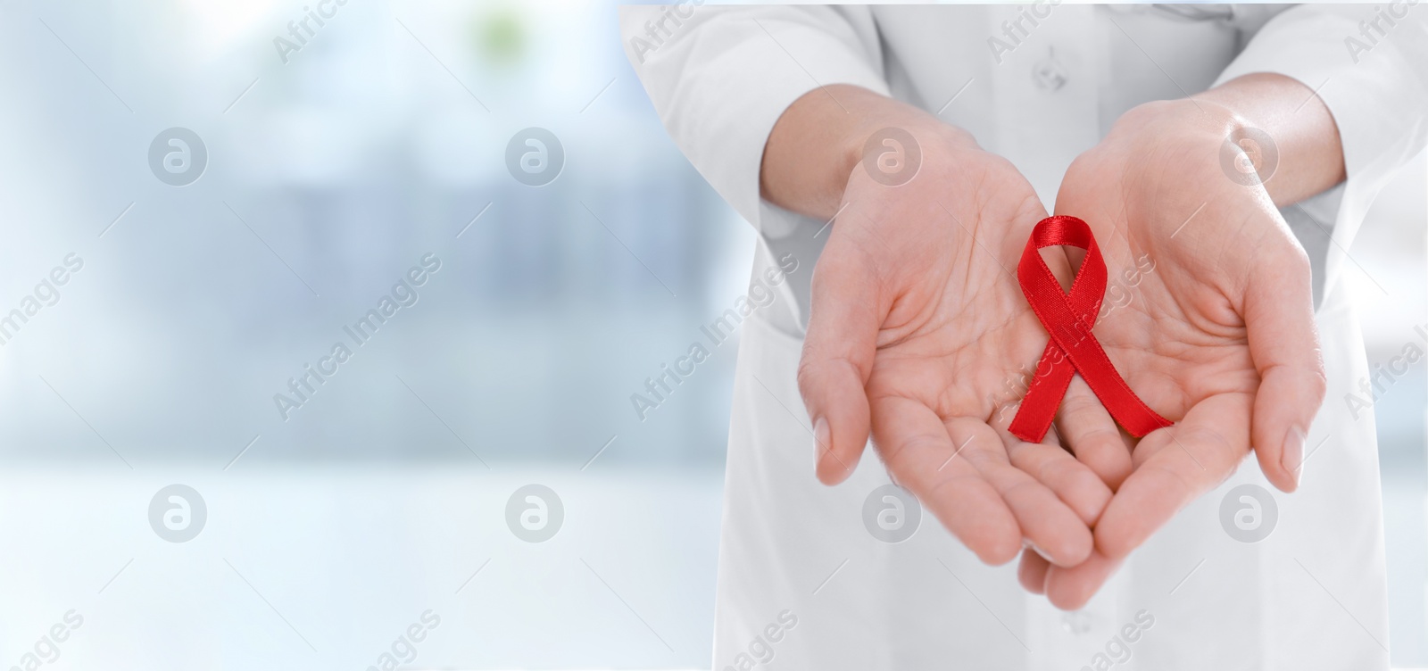 Image of Cancer awareness. Doctor holding red ribbon on blurred background, closeup. Banner design with space for text