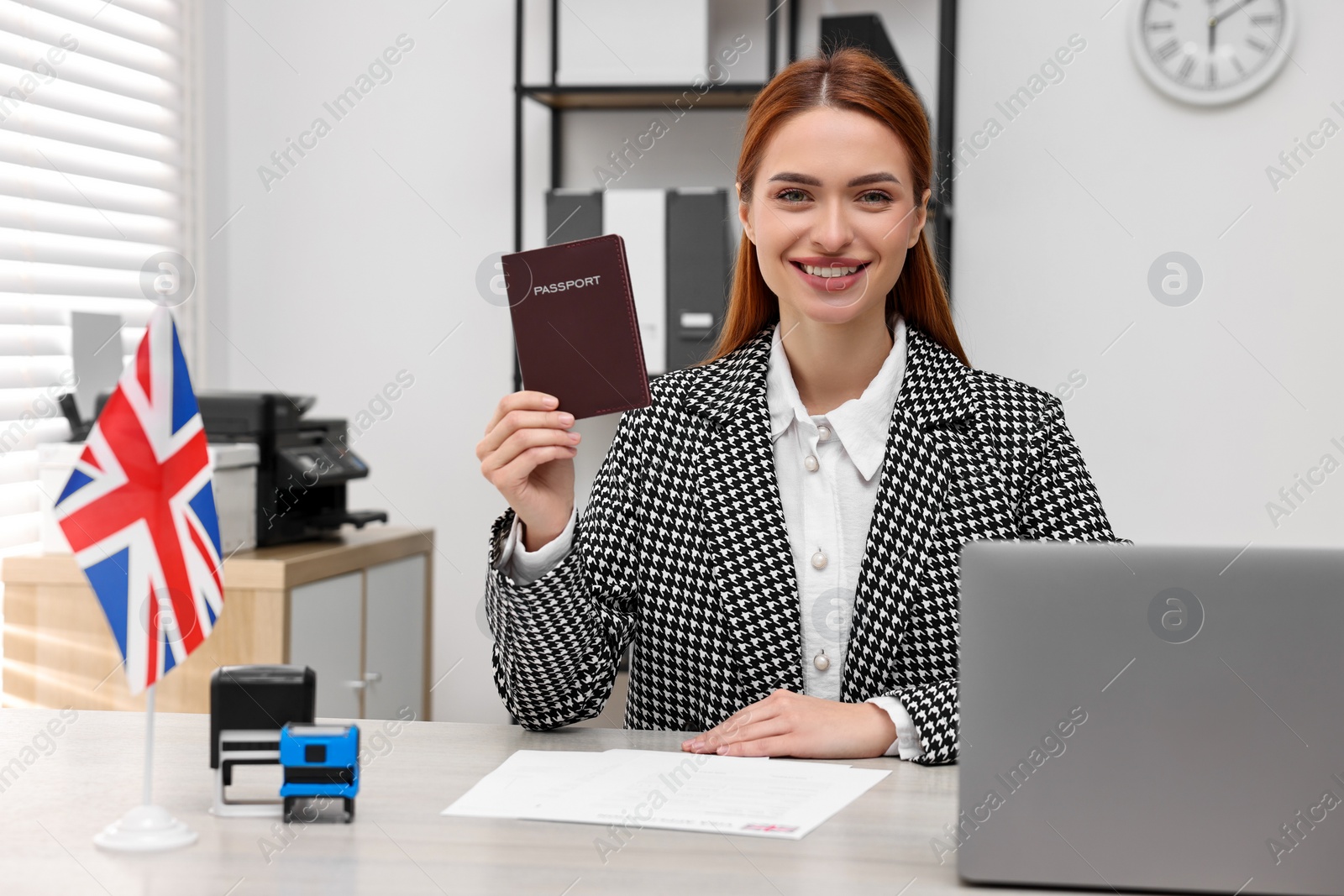 Photo of Immigration to United Kingdom. Smiling embassy worker with passport and documents at table in office