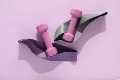 Photo of Dumbbells and fitness elastic bands on violet background, flat lay