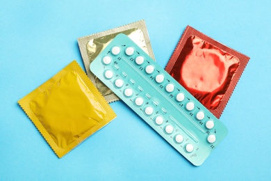 Photo of Condoms and birth control pills on light blue background, flat lay. Safe sex concept