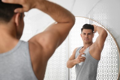 Photo of Handsome man applying deodorant to armpit near mirror in bathroom