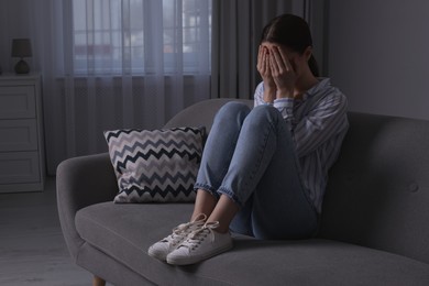 Photo of Unhappy young woman crying on sofa at home, space for text. Loneliness concept