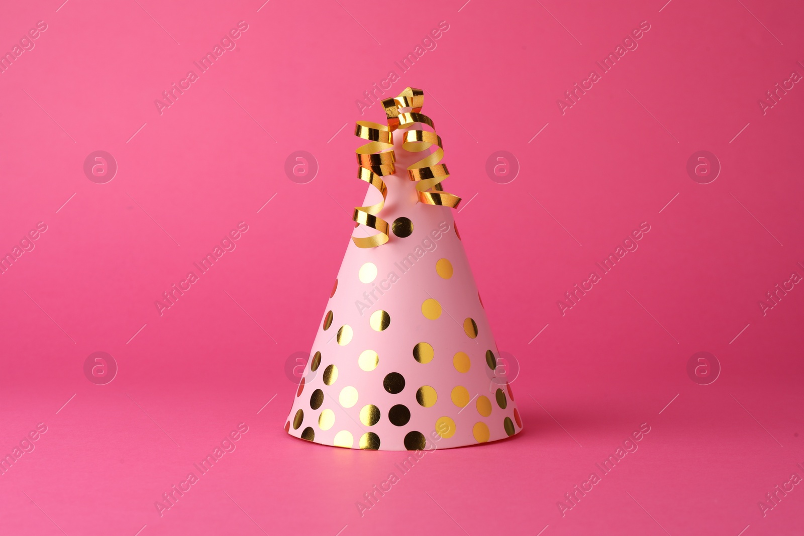 Photo of One beautiful party hat with serpentine streamers on pink background