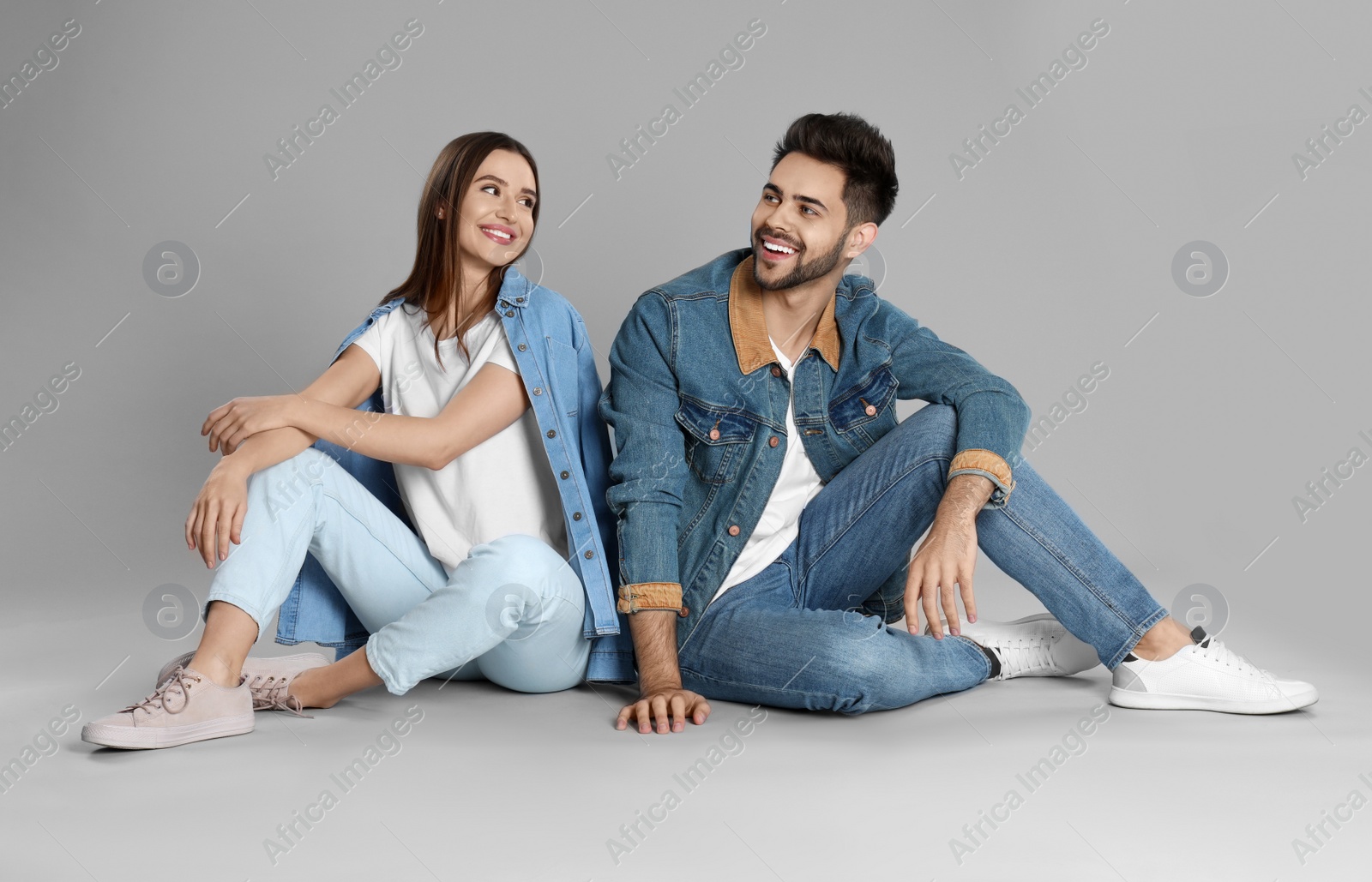 Photo of Young couple in stylish jeans sitting on grey background