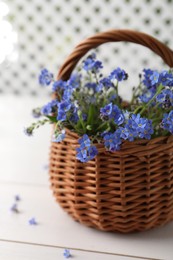 Photo of Beautiful blue forget-me-not flowers in wicker basket on white wooden table