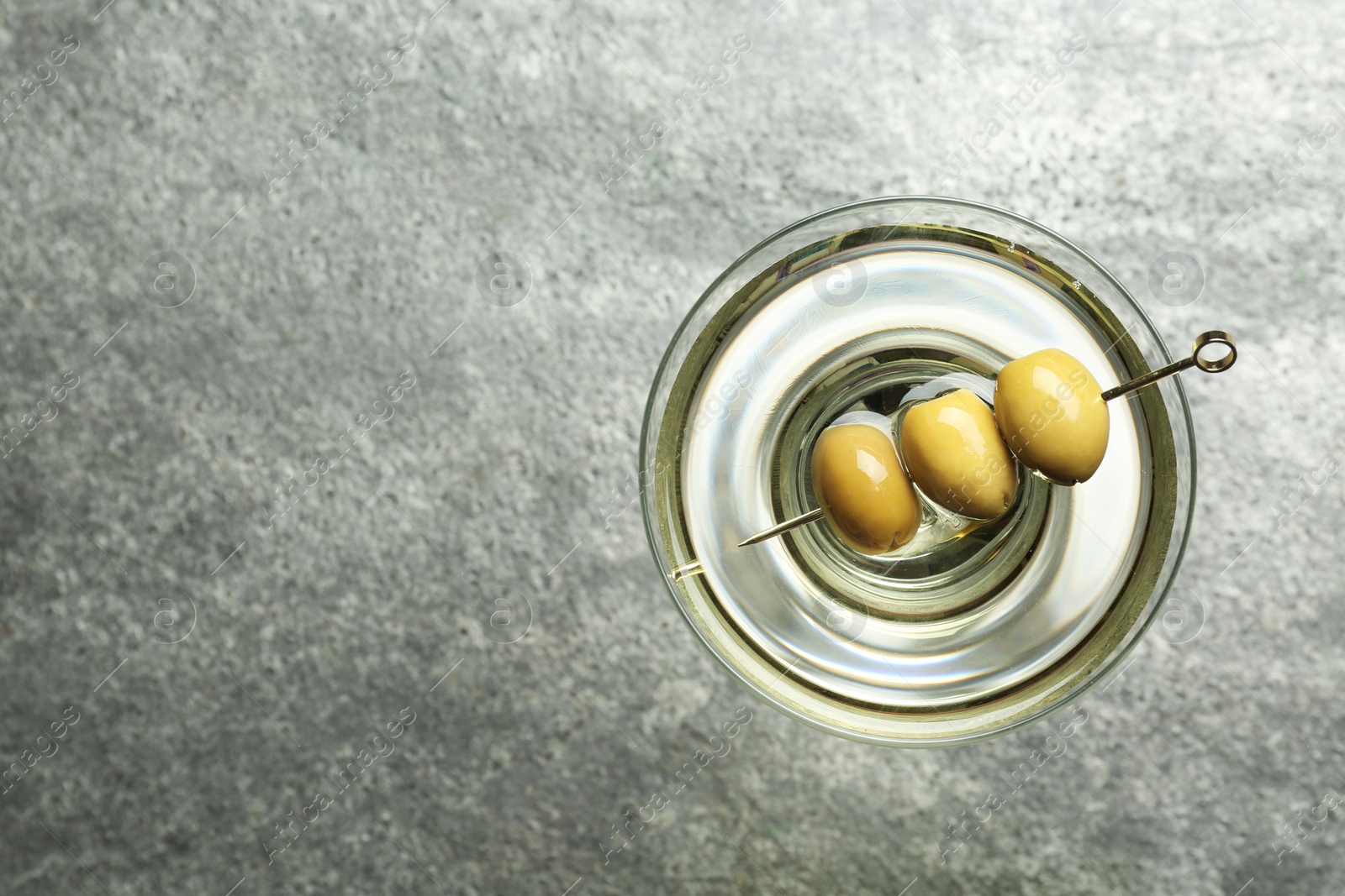 Photo of Martini cocktail with olives on grey table, top view. Space for text