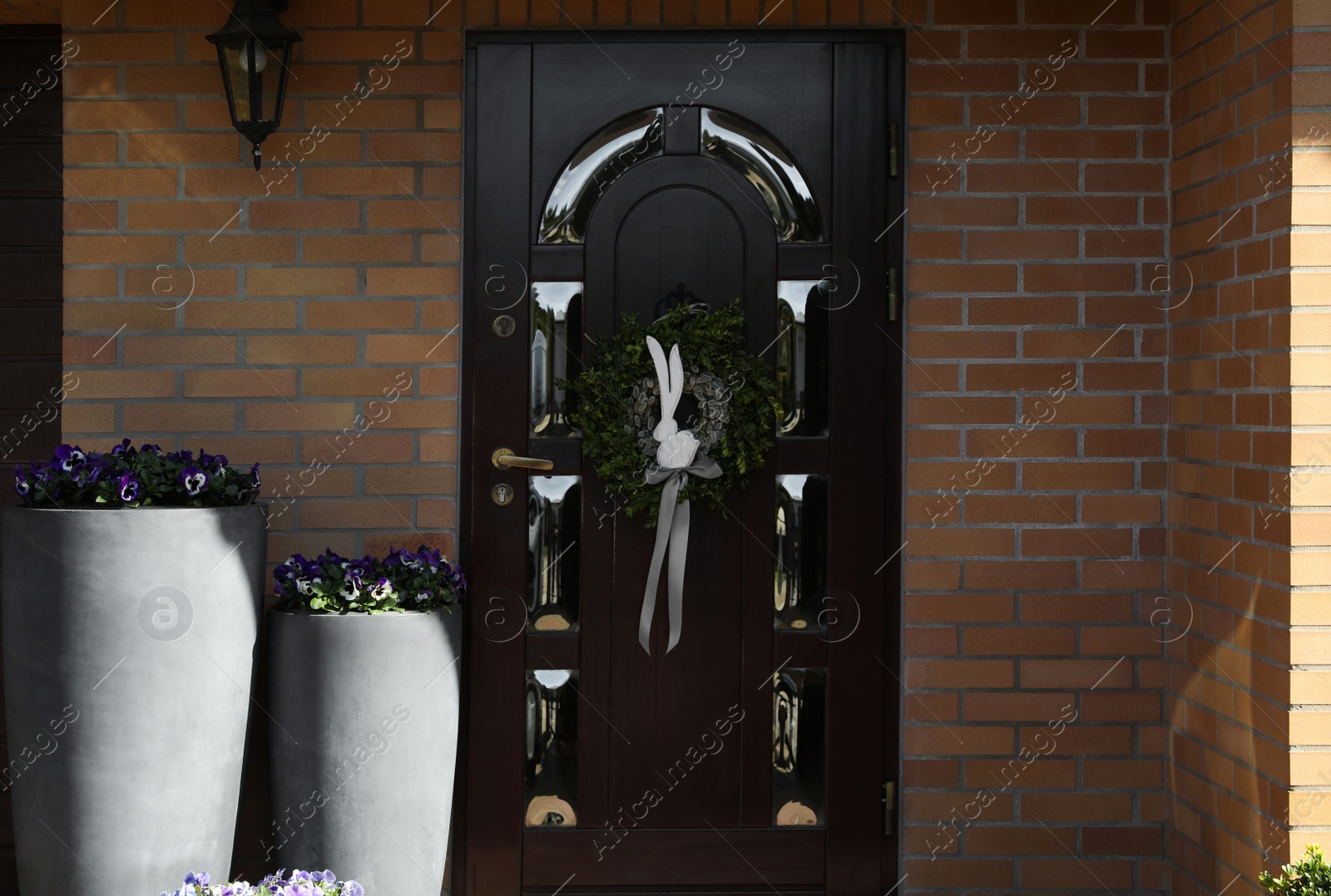 Photo of Beautiful wreath with bunny and bow hanging on door outdoors. Easter celebration