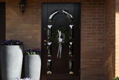 Photo of Beautiful wreath with bunny and bow hanging on door outdoors. Easter celebration