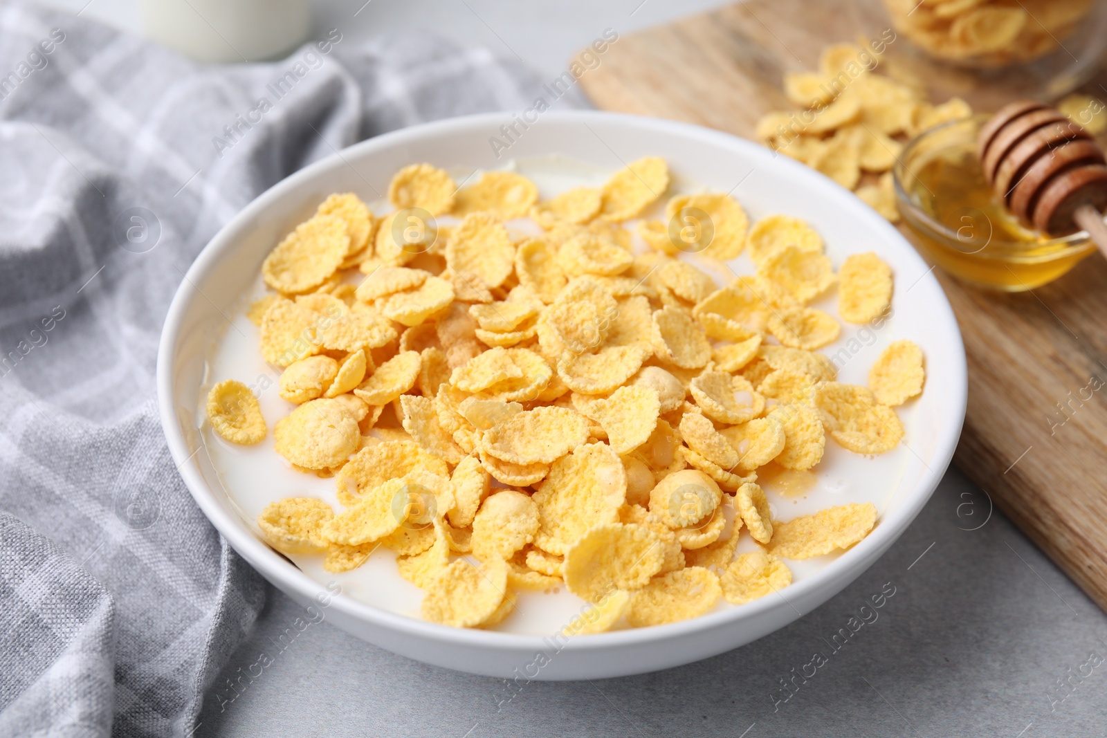 Photo of Breakfast cereal. Corn flakes and milk in bowl on light grey table, closeup