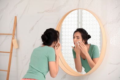 Beautiful young woman with acne problem near mirror in bathroom