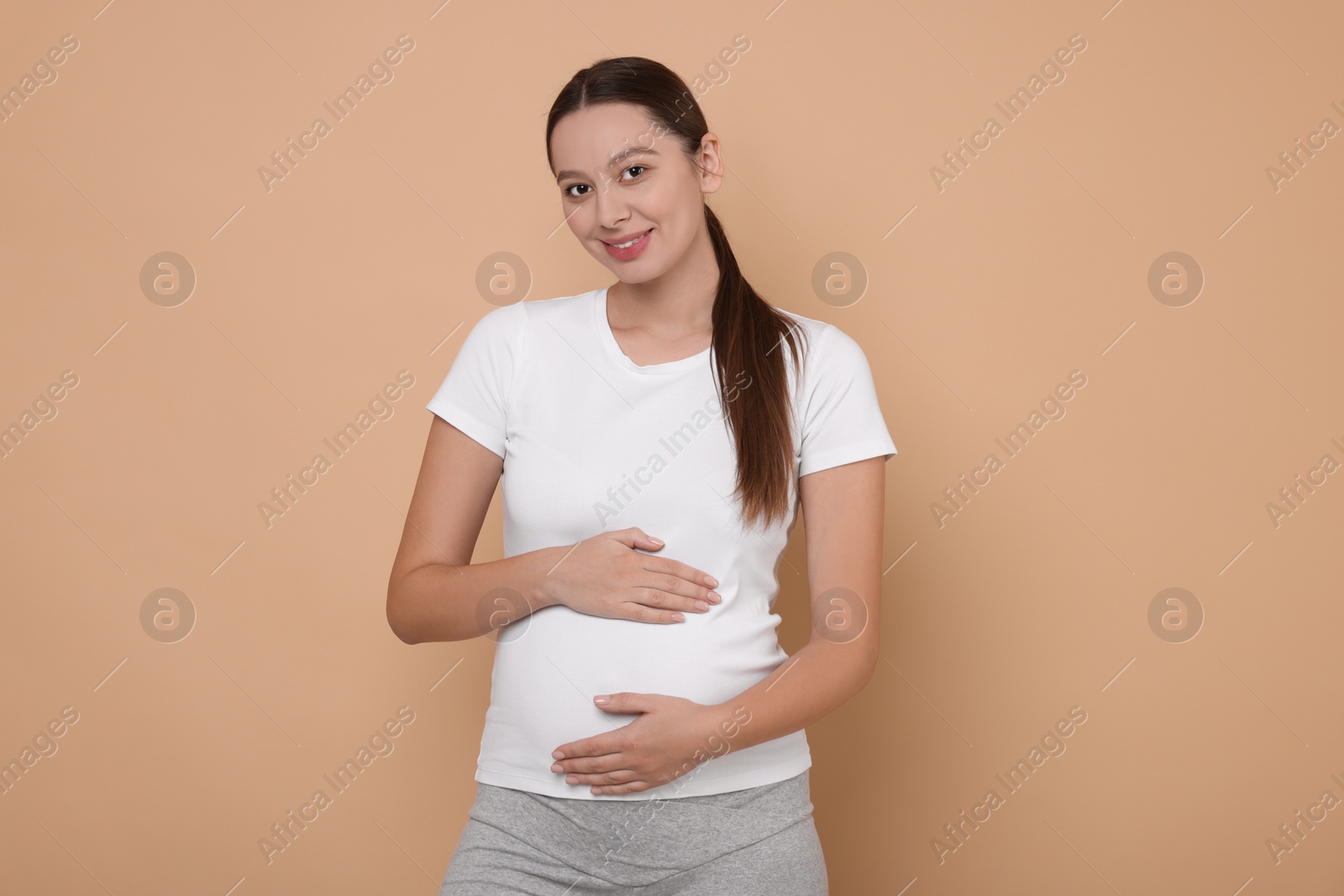 Photo of Beautiful pregnant woman in white T-shirt on beige background