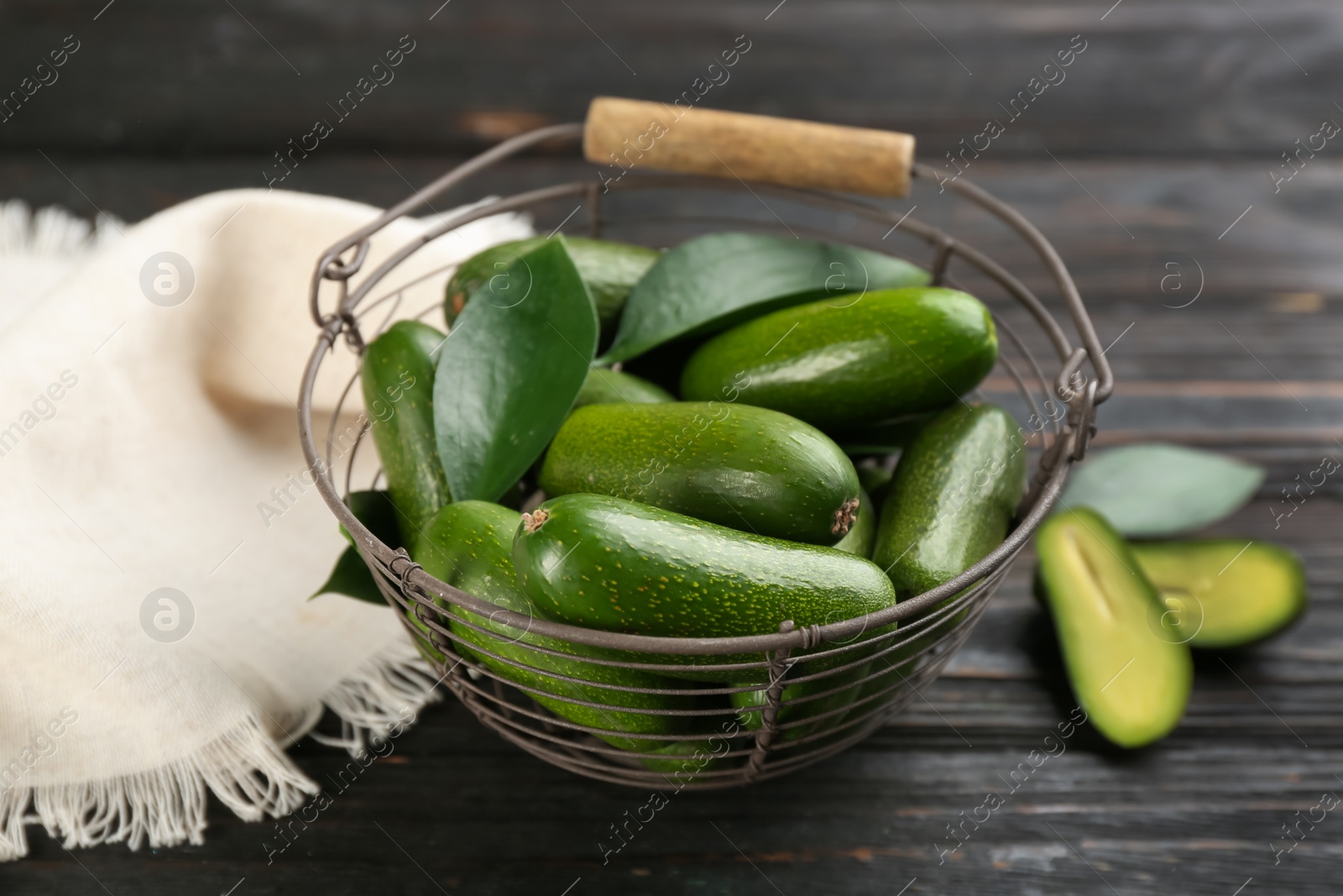 Photo of Fresh seedless avocados in metal basket on dark wooden table