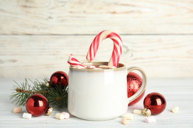 Photo of Cup of tasty cocoa with marshmallows, candy cane and Christmas decor on white wooden table