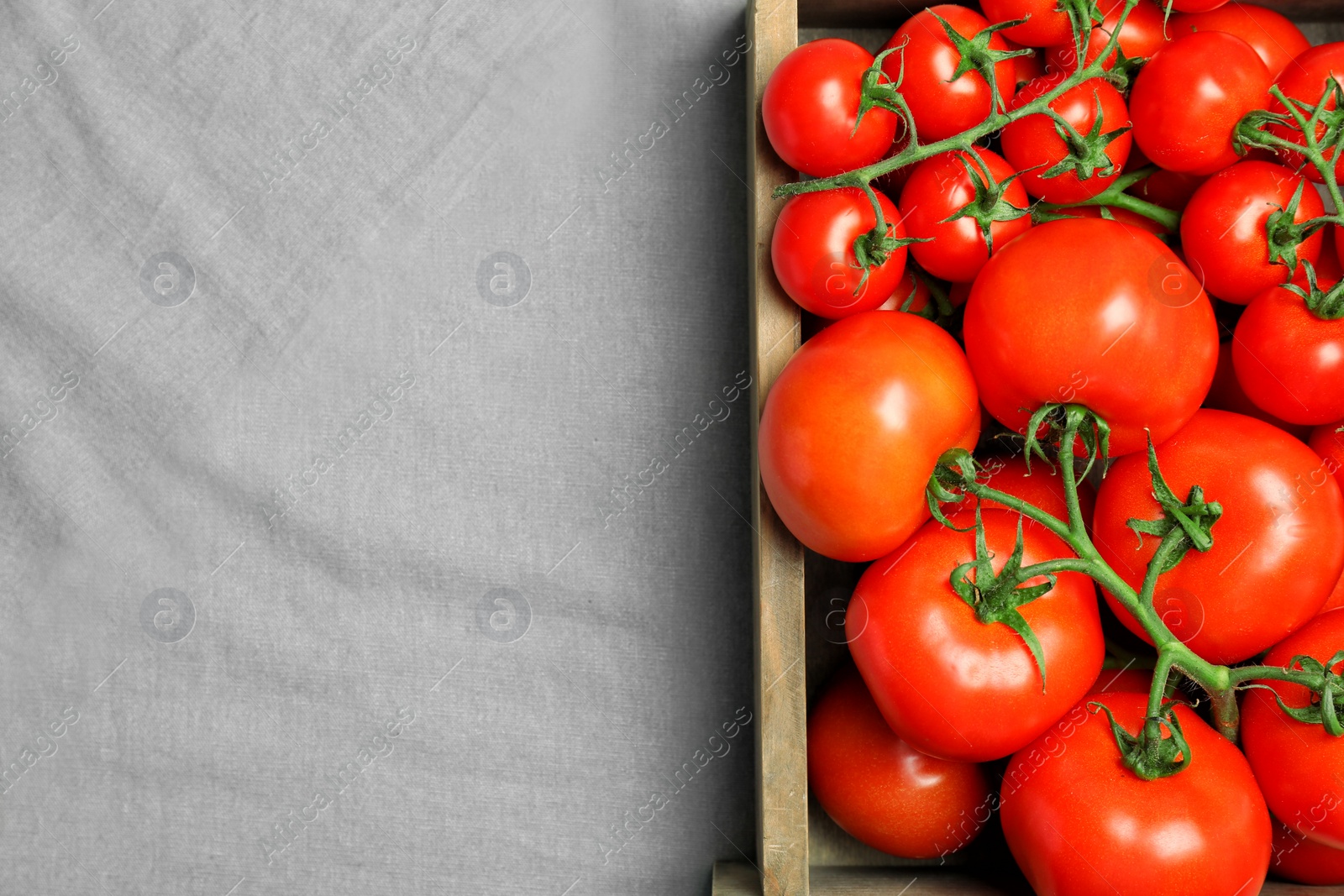 Photo of Wooden crate with fresh ripe tomatoes on grey fabric