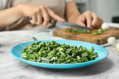 Photo of Plate with chopped green onion and blurred woman on background